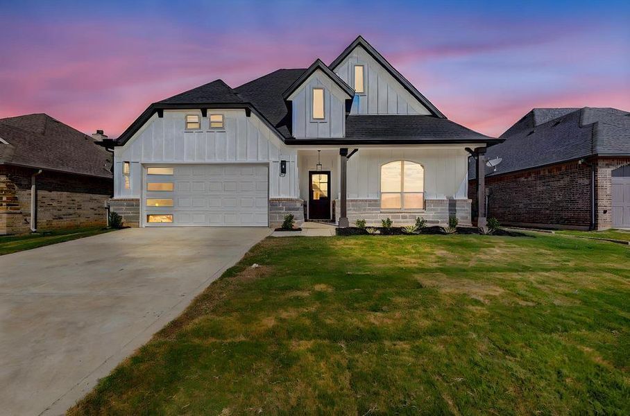 View of front facade featuring board and batten siding, a lawn, concrete driveway, a garage, and roof with shingles