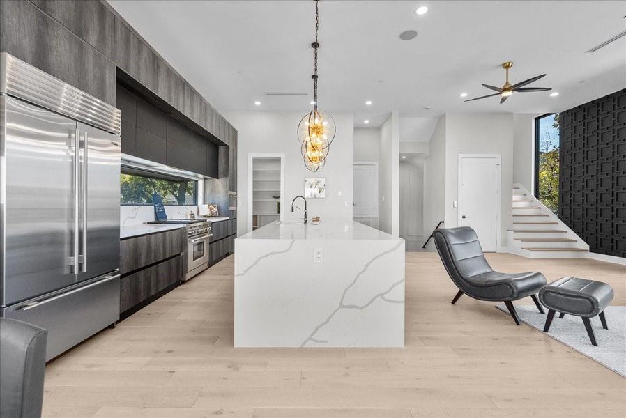 This modern kitchen features sleek dark cabinetry, a spacious marble island, and stainless steel appliances. The open layout connects to a living area with stylish seating and a contemporary staircase, enhancing the home's elegant design. This modern kitchen features sleek dark cabinetry, a spacious marble island, and stainless steel appliances. The open layout connects to a living area with stylish seating and a contemporary staircase, enhancing the home's elegant design.