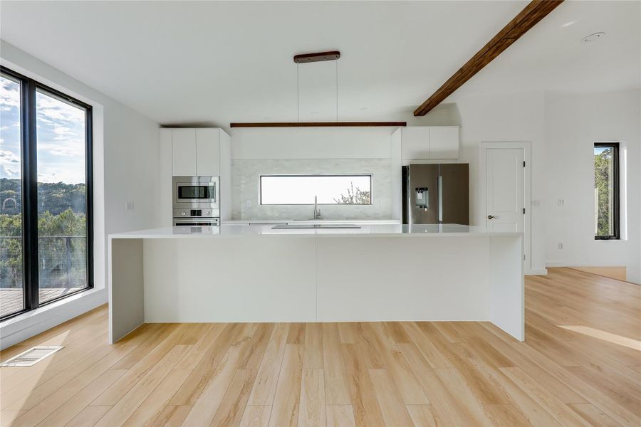 Kitchen featuring white cabinetry, light wood finished floors, stainless steel appliances, modern cabinets, and beam ceiling Kitchen featuring white cabinetry, light wood finished floors, stainless steel appliances, modern cabinets, and beam ceiling