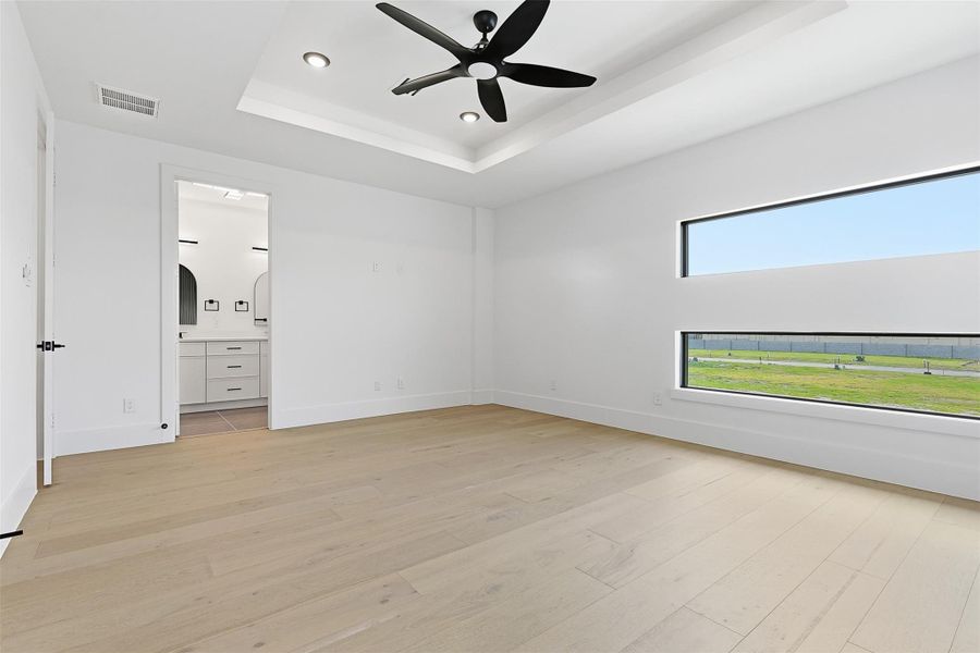 Light wood-look flooring and horizontal black-framed windows characterize the primary suite.