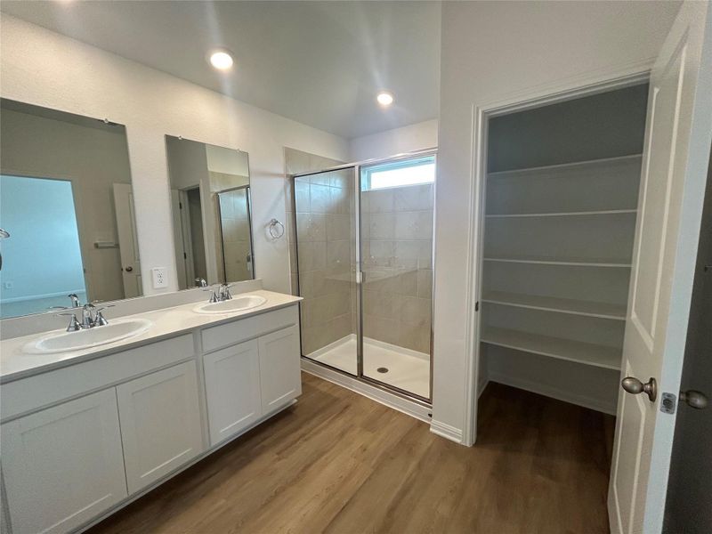 Bathroom featuring wood finished floors, double vanity, and a shower stall