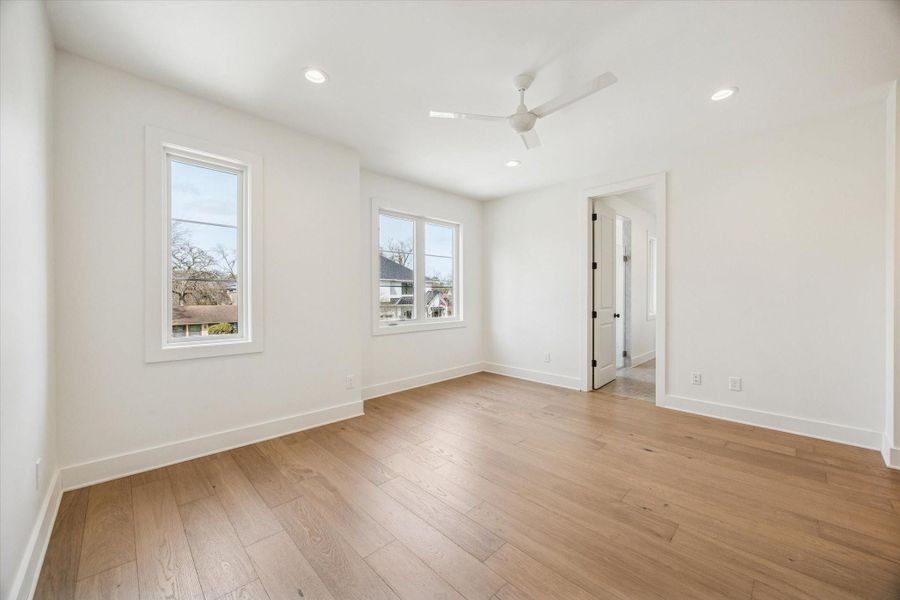 Bright upstairs bedroom features wide plank hardwood floors, recessed lighting, and dual windows that frame treetop views. Convenient access to the nearby bath and game room makes this space ideal for guests or everyday living.