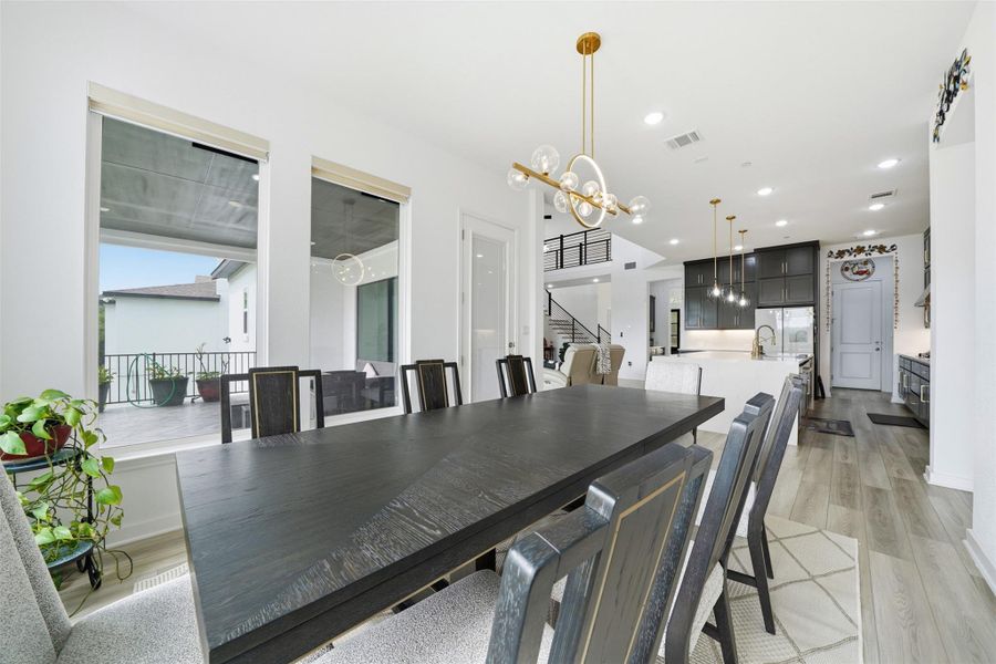 The dining area features a large table, contemporary chandelier, and ample natural light from the expansive windows