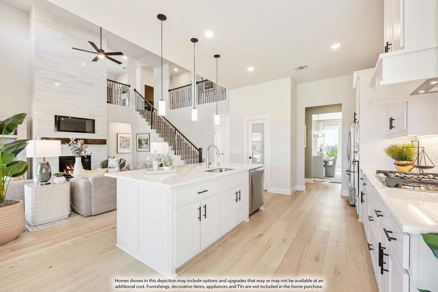 Open-concept kitchen with white island, pendant lights, and view of two-story living room with staircase and fireplace