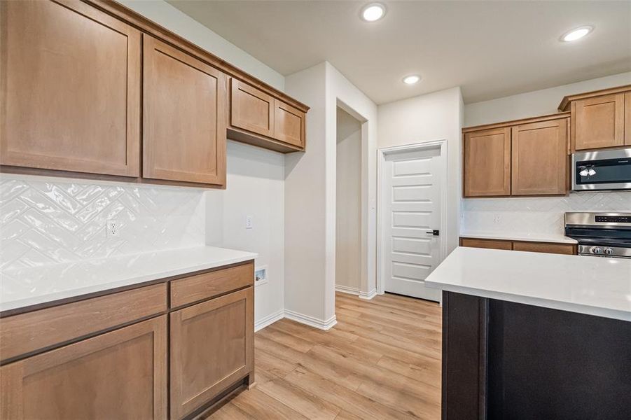 Kitchen with tasteful backsplash, appliances with stainless steel finishes, light stone counters, light wood-type flooring, and brown cabinets