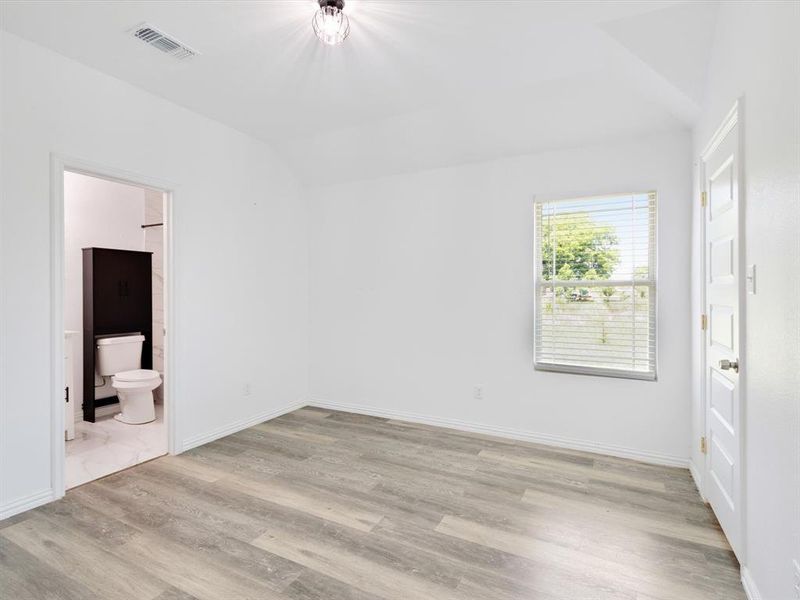 Spacious room featuring wood-finish flooring, a contemporary ceiling light fixture, and a window with horizontal blinds