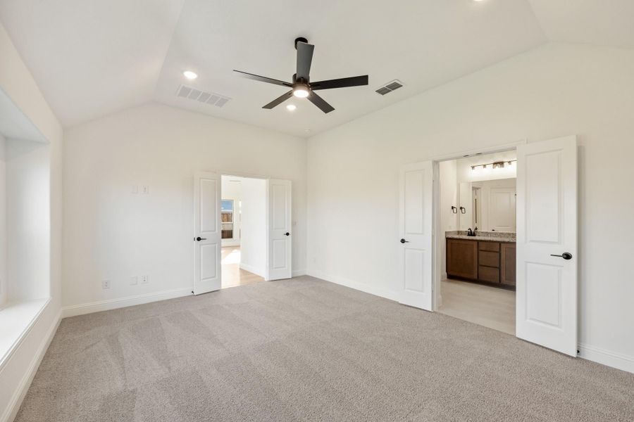 Empty master bedroom with vaulted ceiling, ceiling fan, carpet floors, and ensuite bathroom access Empty master bedroom with vaulted ceiling, ceiling fan, carpet floors, and ensuite bathroom access
