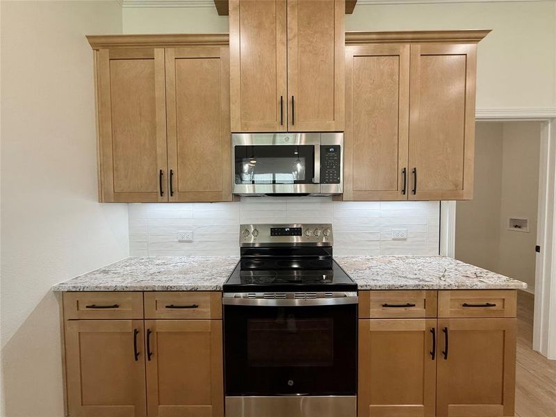 Kitchen with appliances with stainless steel finishes, light stone countertops, decorative backsplash, and light wood finished floors