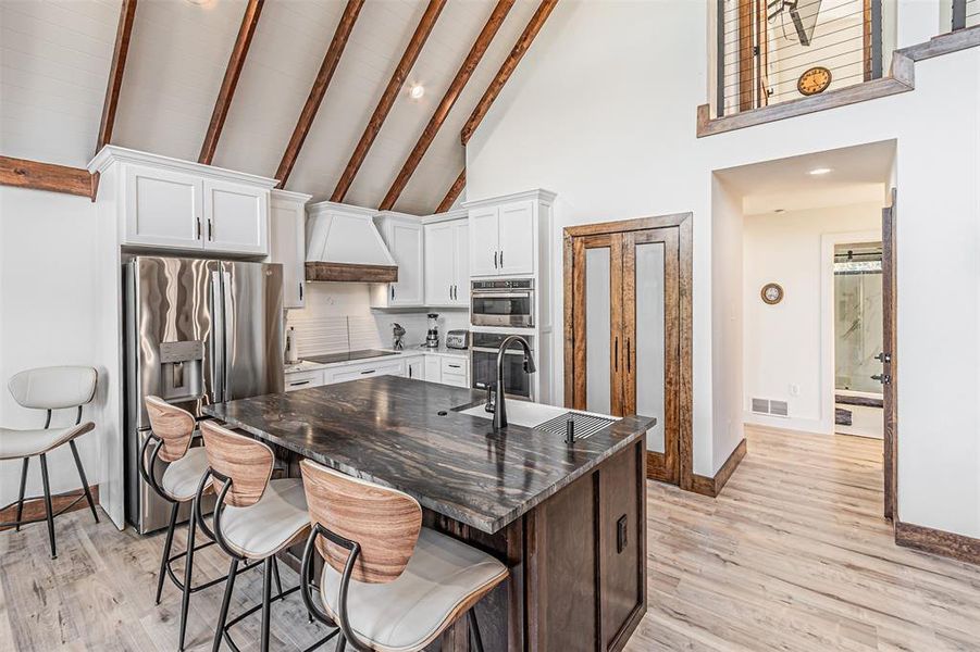Dual tone kitchen with a kitchen breakfast bar, stainless steel appliances, a center island with sink, dark stone counters, and dual tone cabinetry