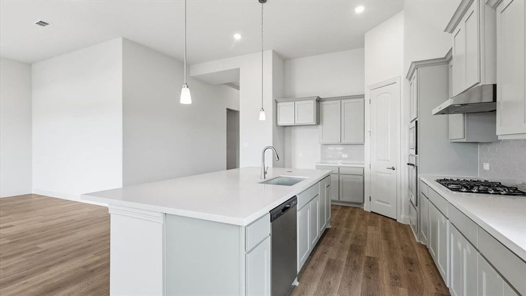 Contemporary kitchen featuring a large island with a sink and pendant lighting, light gray cabinetry, stainless steel appliances, and wood-finish flooring