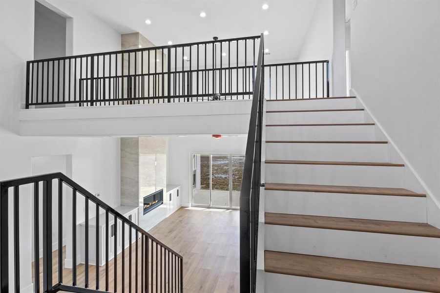 Staircase featuring recessed lighting, wood finished floors, a tile fireplace, and a towering ceiling Staircase featuring recessed lighting, wood finished floors, a tile fireplace, and a towering ceiling