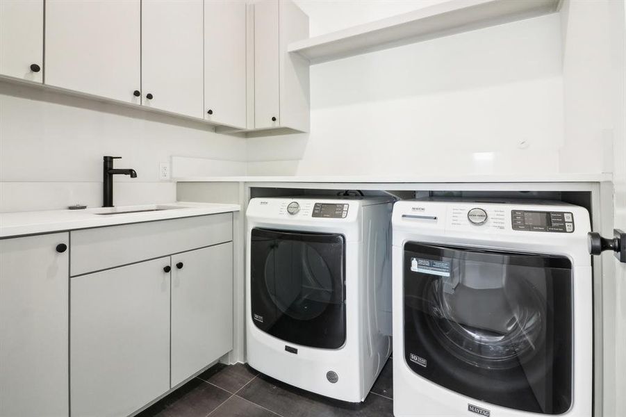 Laundry area featuring sink, dark tile patterned flooring, cabinets, and separate washer and dryer