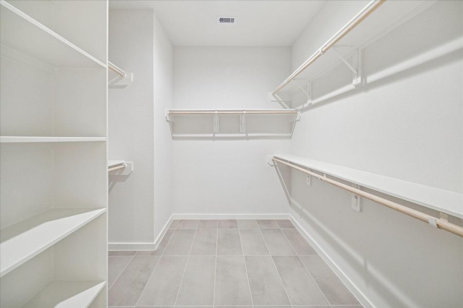 Generous walk-in closet with built-in shelving and multiple hanging sections, providing ample storage and organization options within a bright, open layout.