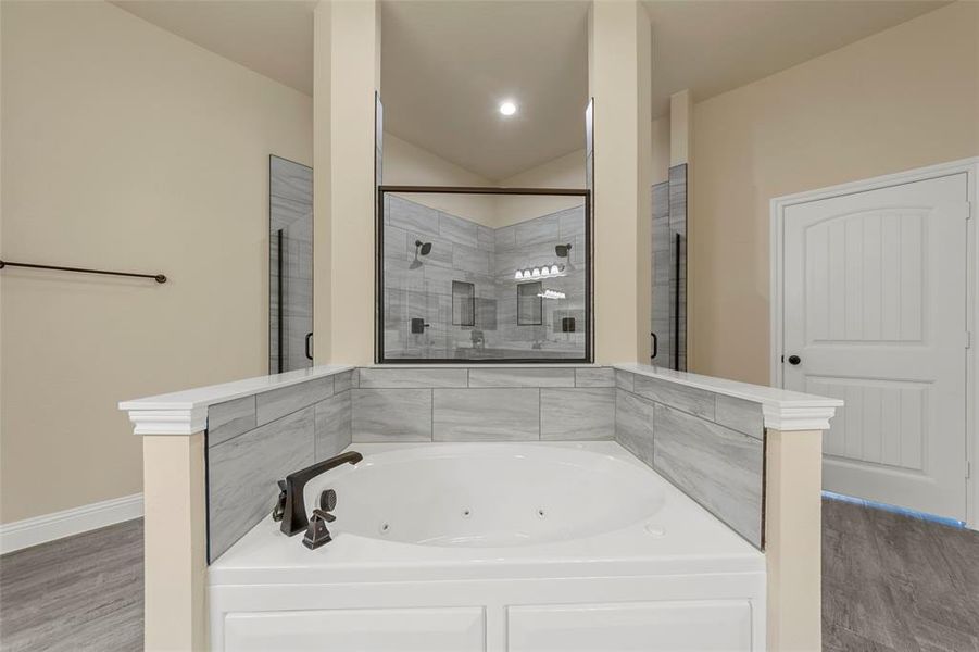 Full bathroom featuring a stall shower, a tub with jets, wood finished floors, lofted ceiling, and baseboards