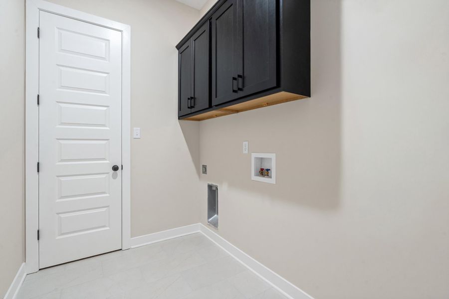 Utility room featuring dark cabinetry with matte black hardware, light neutral wall paint, and light-colored tile flooring Utility room featuring dark cabinetry with matte black hardware, light neutral wall paint, and light-colored tile flooring