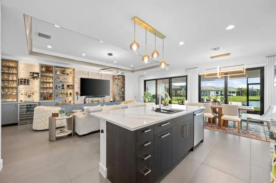 Center island with quartz countertop and undermount sink, dark-toned cabinetry, built-in display shelving with integrated lighting, oversized sliding glass doors, and recessed ceiling lighting