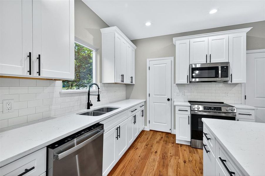 Kitchen featuring white cabinetry, light stone countertops, appliances with stainless steel finishes, light wood-type flooring, and tasteful backsplash Kitchen featuring white cabinetry, light stone countertops, appliances with stainless steel finishes, light wood-type flooring, and tasteful backsplash