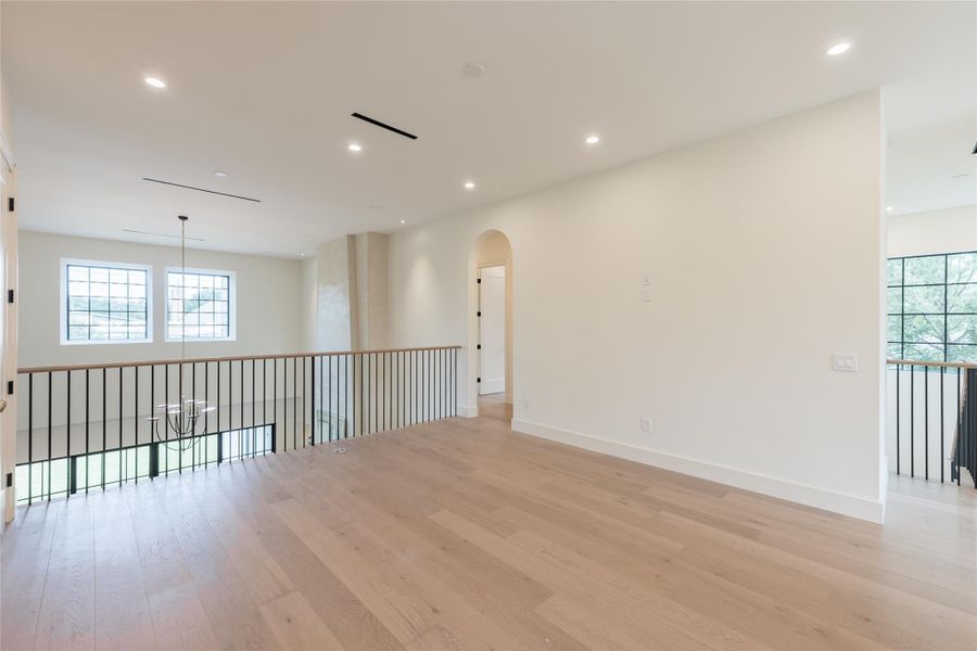 The second-floor flex space overlooks the dramatic two-story living room, framed by custom iron railings and natural light pouring in from large-scale windows. An arched passageway and European white wide oak flooring continue the home's signature design language. The second-floor flex space overlooks the dramatic two-story living room, framed by custom iron railings and natural light pouring in from large-scale windows. An arched passageway and European white wide oak flooring continue the home's signature design language.