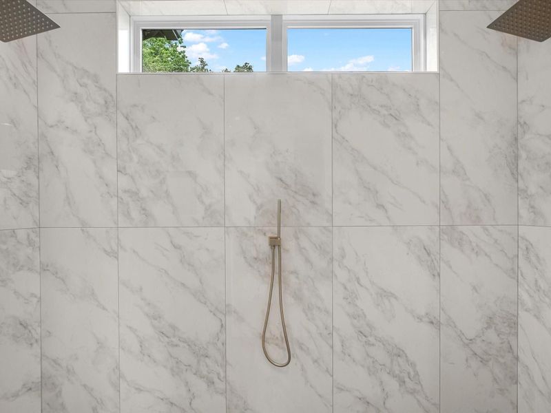 Oversized walk-in shower with floor-to-ceiling tile, dual showerheads, and natural light.