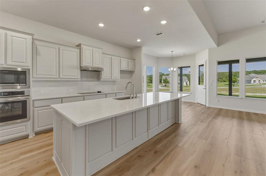 Gourmet kitchen with extensive light-toned cabinetry, stainless steel appliances, and a central island featuring a sink Gourmet kitchen with extensive light-toned cabinetry, stainless steel appliances, and a central island featuring a sink