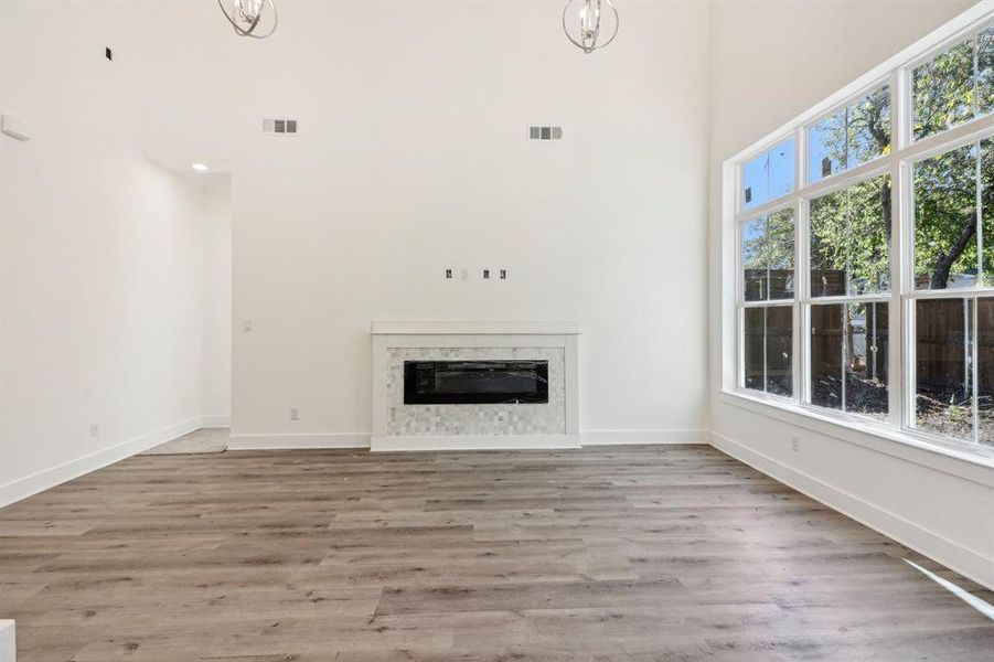 Unfurnished living room with a fireplace, light wood finished floors, and a towering ceiling