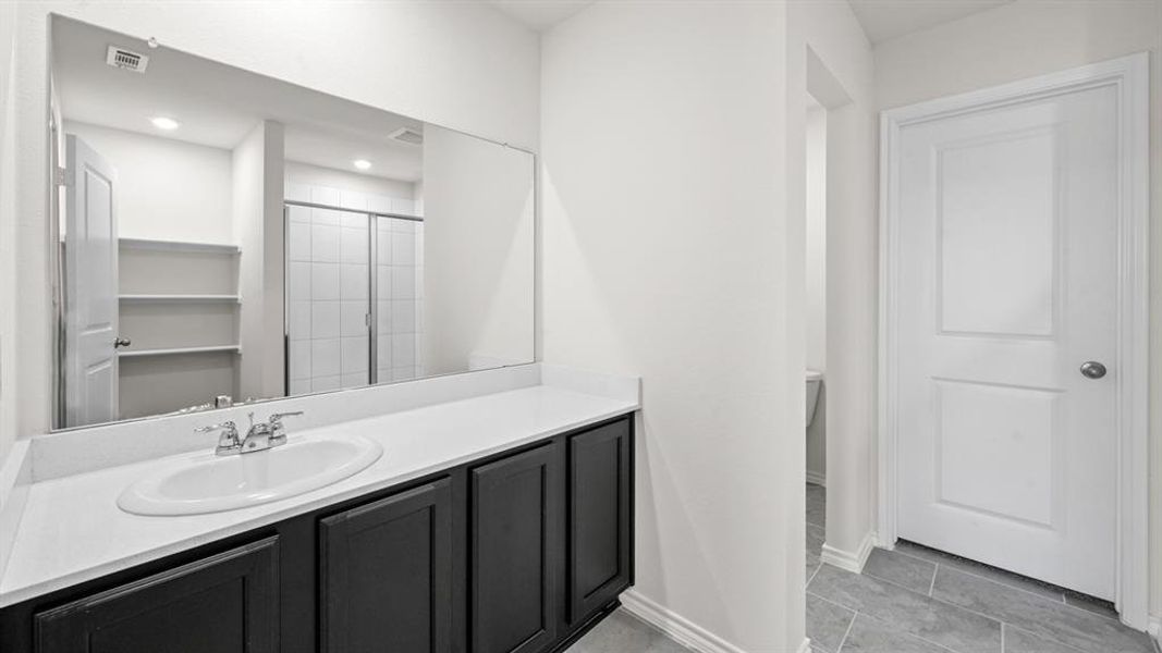 Bathroom vanity featuring a white oval sink set in a light-toned countertop, dark cabinetry, and a large wall-mounted mirror