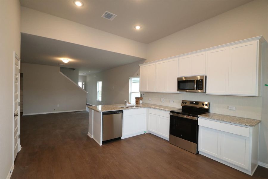 Kitchen featuring white cabinets, dark wood-type flooring, light stone countertops, and stainless steel appliances