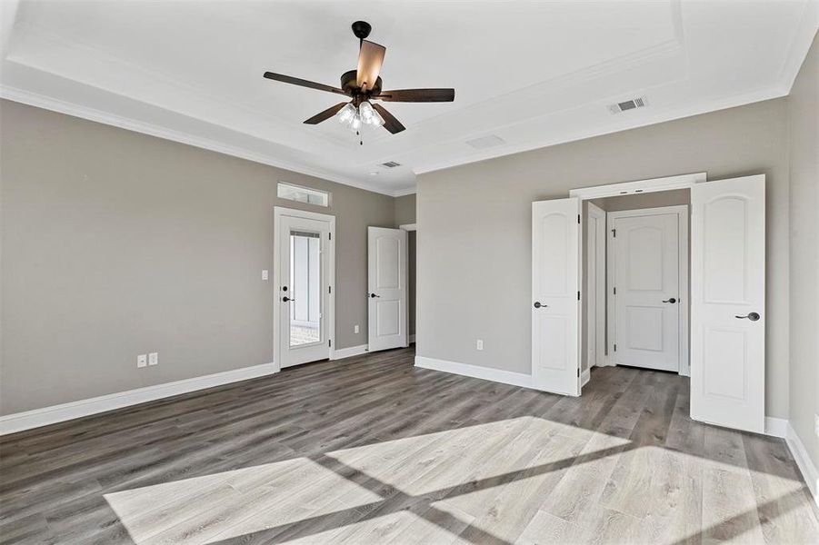 Unfurnished bedroom with ceiling fan, a tray ceiling, light hardwood / wood-style flooring, and crown molding