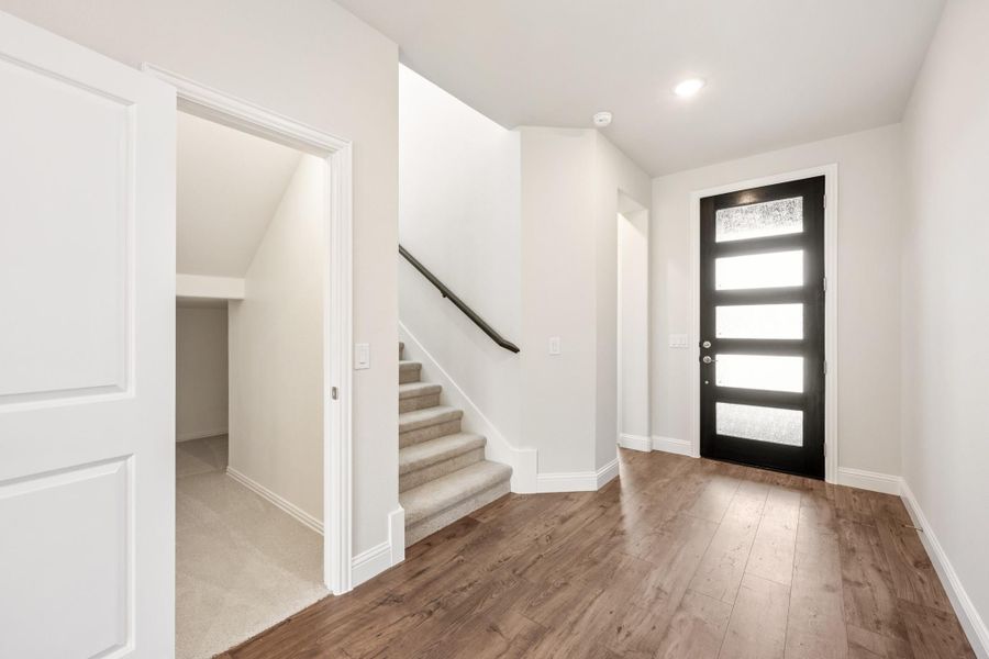 Entryway with hardwood floors, black front door with glass panels, and carpeted staircase nearby Entryway with hardwood floors, black front door with glass panels, and carpeted staircase nearby