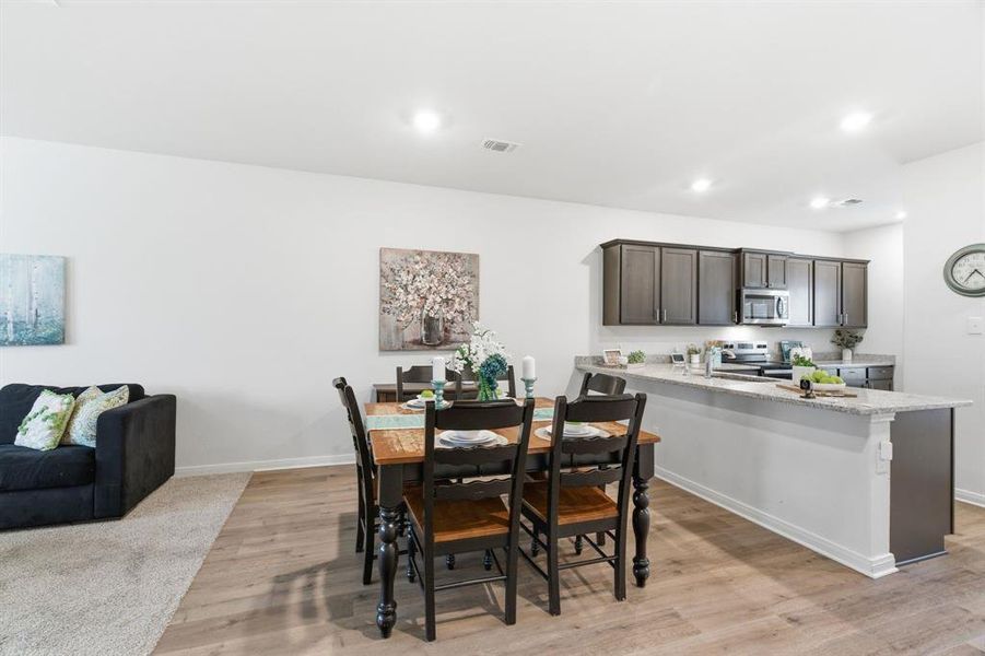 This open-concept area features a kitchen with dark cabinetry, stainless steel appliances, and a light-colored countertop, alongside a dining space with a wooden table and seating