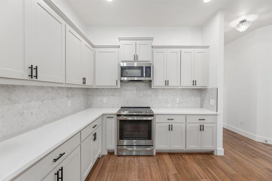 Kitchen with backsplash, appliances with stainless steel finishes, light countertops, and wood finished floors