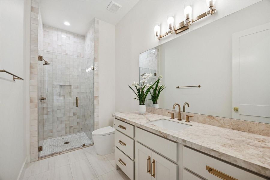 Hall bath located on the second-floor features porcelain countertop, porcelain tile, plus a polished marble mosaic tile in the glass enclosed shower.