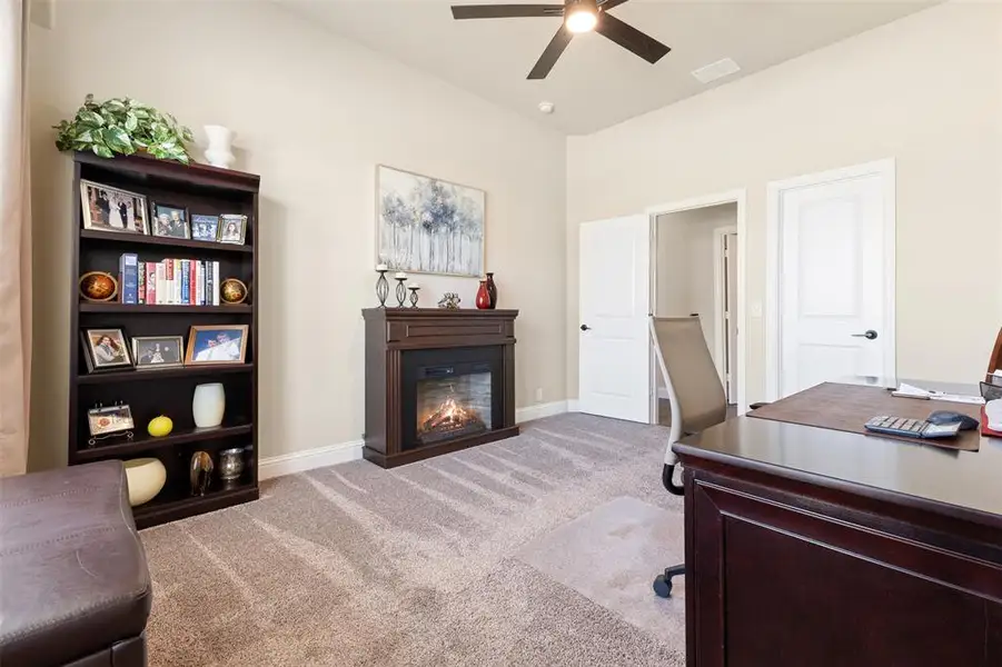 Carpeted room featuring a built-in fireplace, vaulted ceiling, and a ceiling fan Carpeted room featuring a built-in fireplace, vaulted ceiling, and a ceiling fan