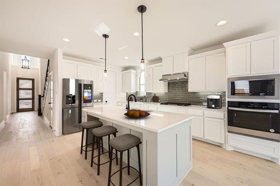 Virtually Staged Photo Kitchen with stainless steel appliances, light wood-style floors, a breakfast bar area, recessed lighting, and an island with sink