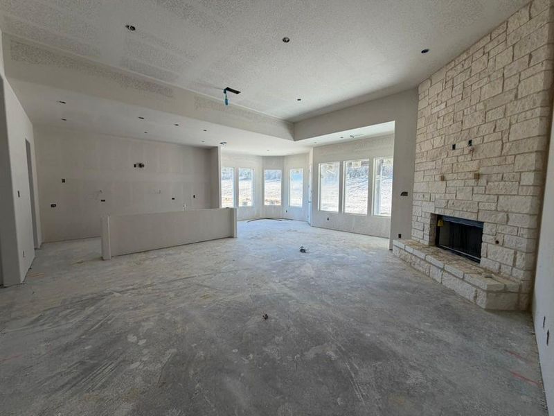 Unfurnished living room with a stone fireplace, a textured ceiling, and unfinished concrete floors