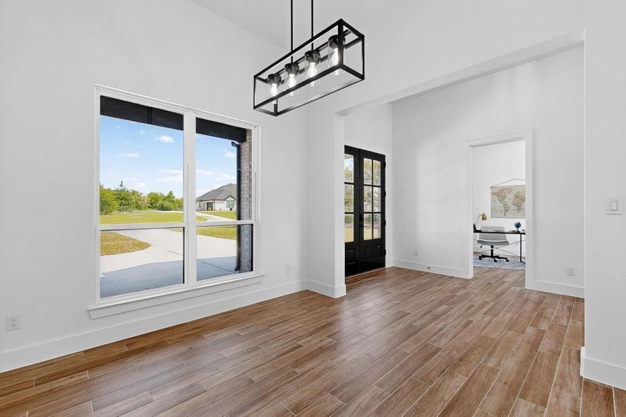 Unfurnished dining area featuring french doors, wood finished floors, and a towering ceiling