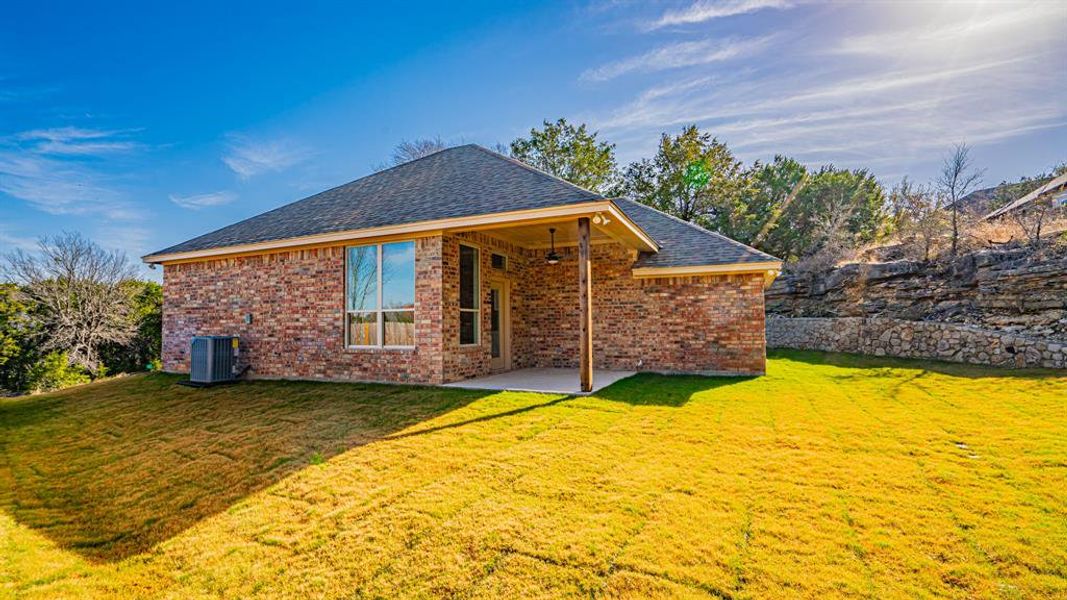 Back of property featuring brick siding, a lawn, a patio area, and roof with shingles