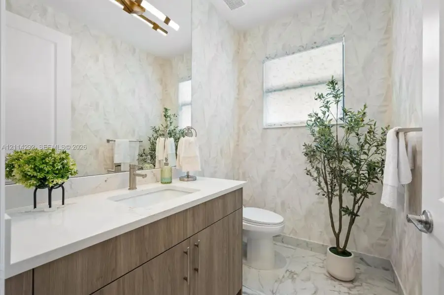 Bathroom featuring a wood-finish vanity with a stone-surface countertop, rectangular undermount sink, patterned wall covering, and polished stone-finish floor tile