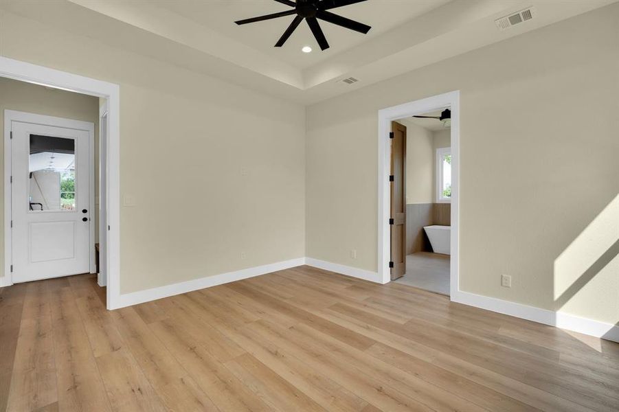 Unfurnished room with ceiling fan, light hardwood / wood-style flooring, and a raised ceiling