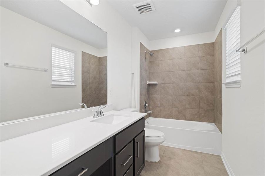 Secondary bath features tile flooring, bath/shower combo with tile surround, stained wood cabinets, beautiful light countertops, mirror, sleek fixtures and modern finishes.