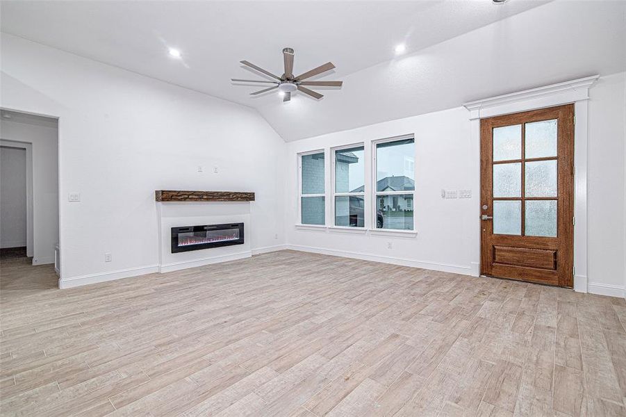 Unfurnished living room featuring a ceiling fan, vaulted ceiling, healthy amount of natural light, light wood-style floors, and a glass covered fireplace Unfurnished living room featuring a ceiling fan, vaulted ceiling, healthy amount of natural light, light wood-style floors, and a glass covered fireplace