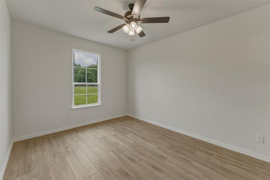 Spacious room with wood-finish flooring, light neutral wall paint, and a ceiling fan with integrated lighting Spacious room with wood-finish flooring, light neutral wall paint, and a ceiling fan with integrated lighting