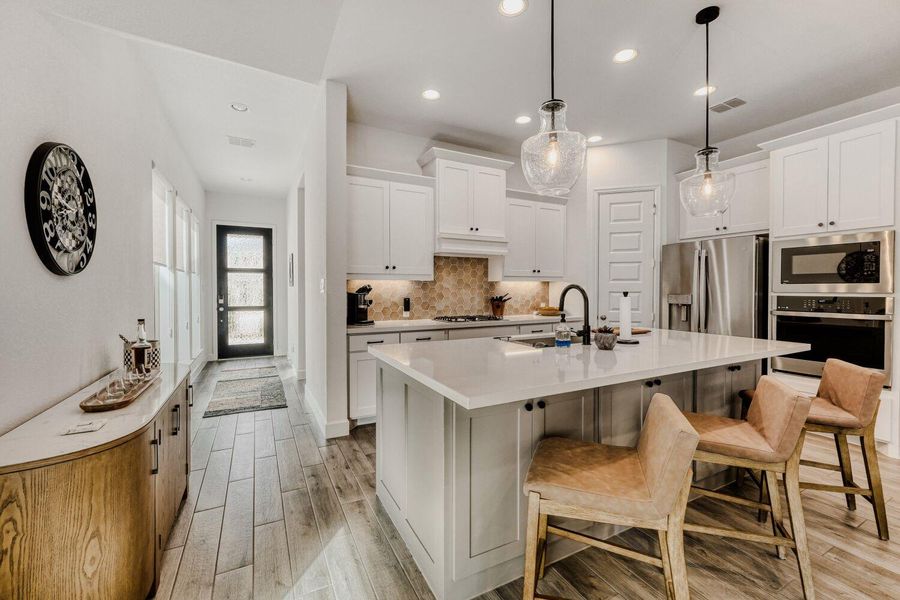 Kitchen with light wood finished floors, stainless steel appliances, a kitchen island with sink, hanging light fixtures, and a kitchen breakfast bar