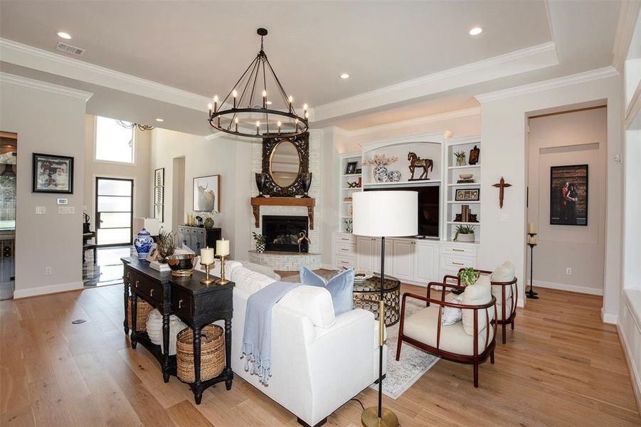 This photo showcases a spacious living room with elegant decor. It features a large chandelier, built-in shelves, a cozy fireplace, and a mix of modern and classic furniture. The room has ample natural light, a neutral color palette, and high ceilings, creating an inviting and stylish atmosphere.