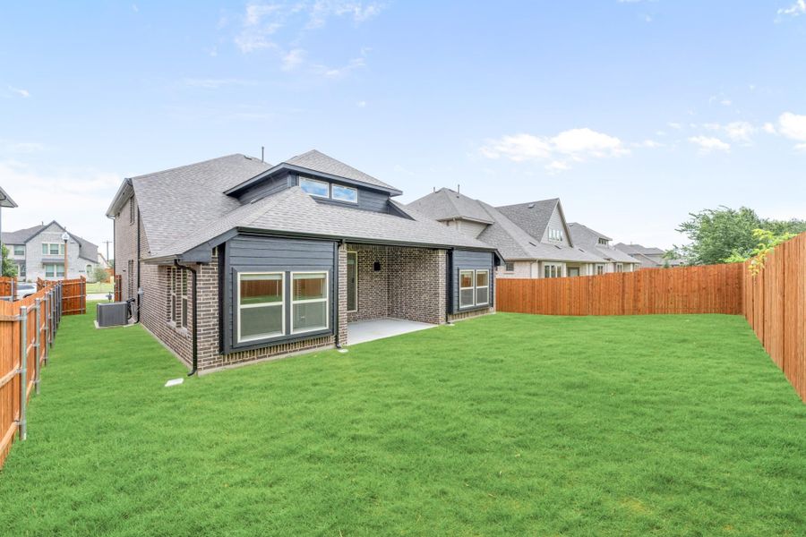 Rear view of brick home with dark trim, covered patio, large grassy backyard, and wood privacy fence Rear view of brick home with dark trim, covered patio, large grassy backyard, and wood privacy fence