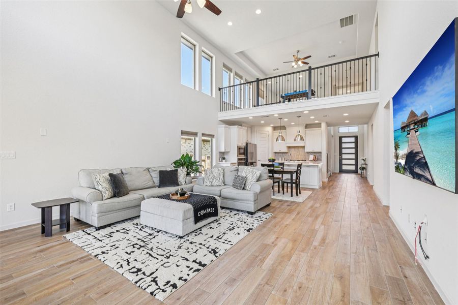 The open-concept living space features light-toned hardwood flooring, high ceilings, and a second-story balcony overlook