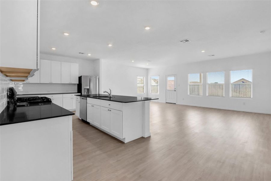 Kitchen featuring white cabinets, stainless steel appliances, open floor plan, light wood finished floors, and tasteful backsplash