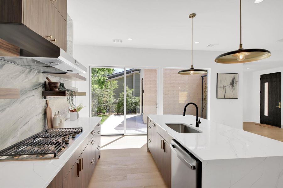 Kitchen with light stone countertops, modern cabinets, light wood-type flooring, stainless steel appliances, and an island with sink