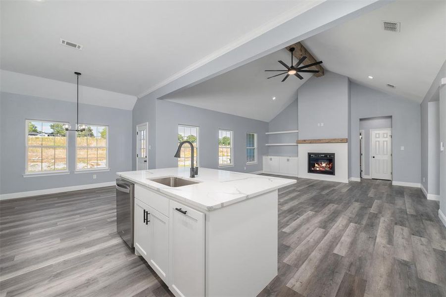 Kitchen featuring white cabinetry, open floor plan, high vaulted ceiling, a glass covered fireplace, and light stone countertops Kitchen featuring white cabinetry, open floor plan, high vaulted ceiling, a glass covered fireplace, and light stone countertops
