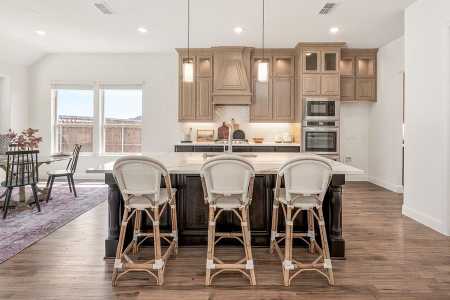 Kitchen with large dark island, three wicker barstools, tan cabinets, and hardwood floors